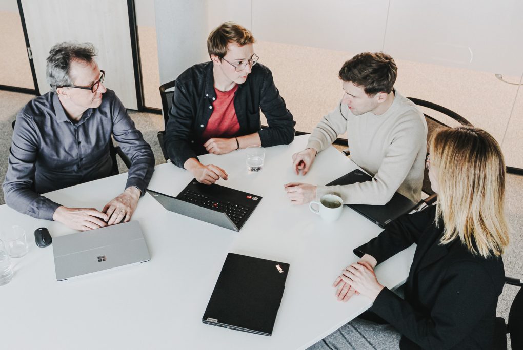 A team of four sitting at a meeting table in discussion.